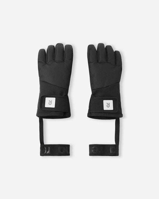 Flat lay view of the backs of the classic black Reima Hanskas kids' ski gloves. The image highlights the waterproof technical fabric, an easy-to-use hook-and-loop adjustable wrist strap for a secure fit, and attached elastic safety wrist leashes.