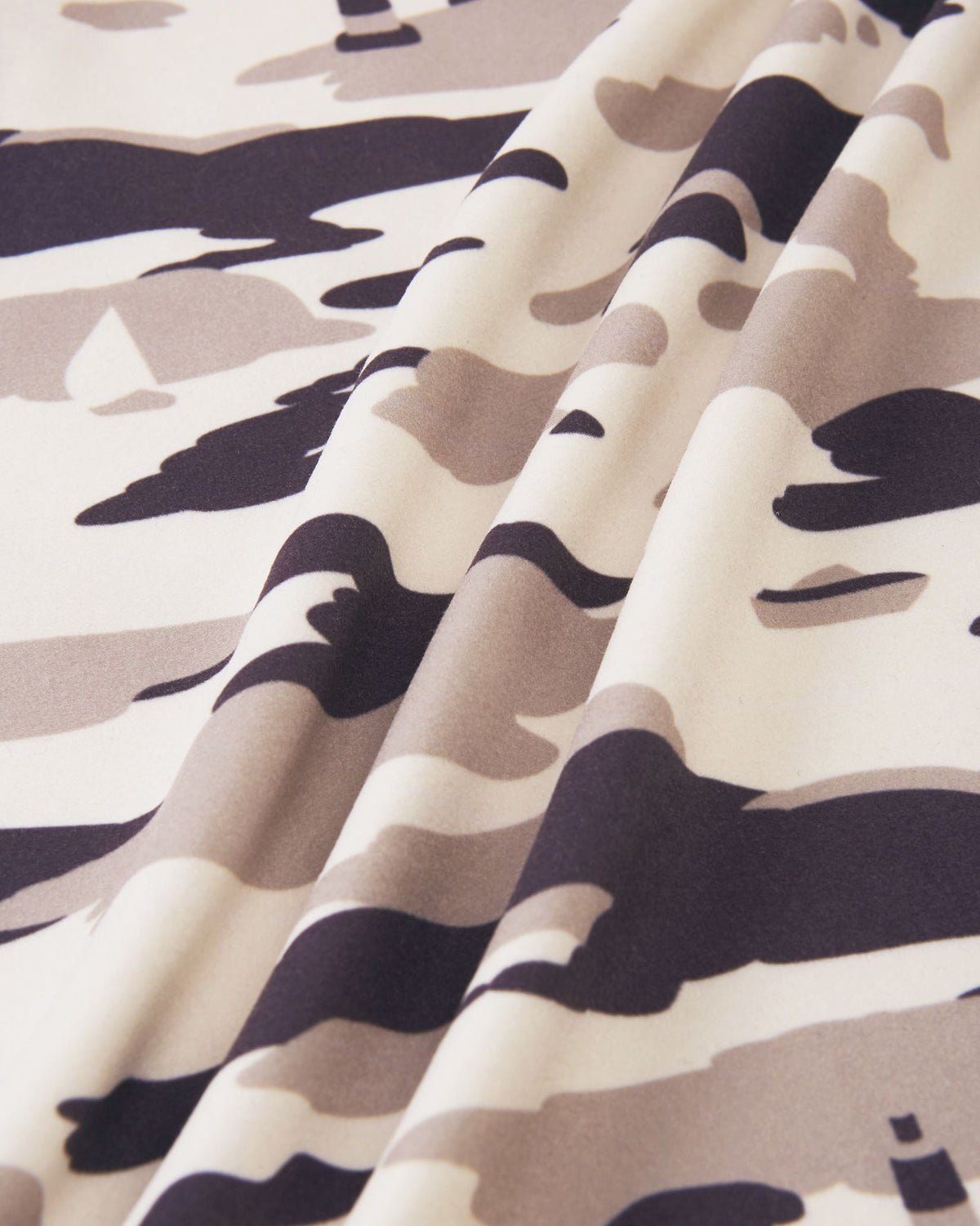 Macro close-up of the high-quality, smooth fleece material on the earthy beige Reima Iisisti kids' jacket, showcasing the neutral grey and tan tones of the distinctive sailboat camo print.