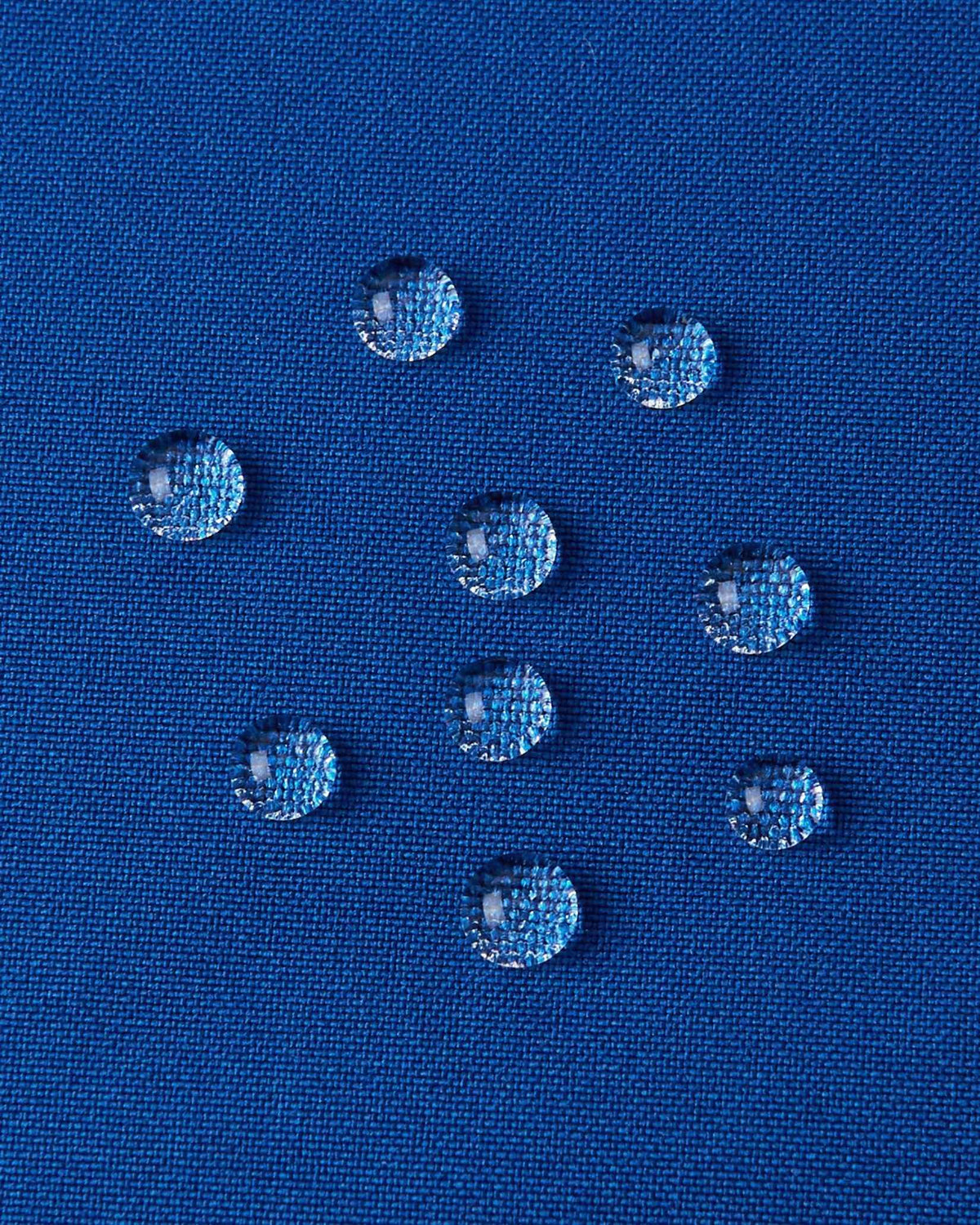 A detailed close-up texture shot of water droplets beading up cleanly on the twilight blue water-repellent fabric of a Reima Kuosku kids ski jacket, demonstrating its durable waterproof performance.