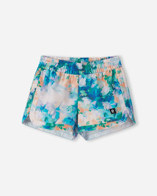 Front view of the Reima Nauru girls' UPF 50+ sunproof swim shorts, featuring a vibrant fresh blue and pastel watercolor floral print, designed with curved hems for comfortable summer mobility.
