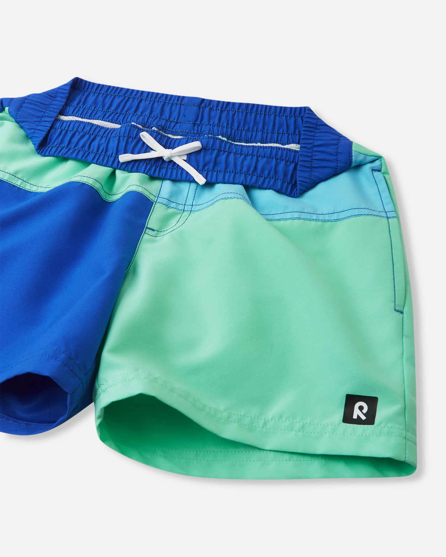 Detailed view of the Reima Palmu kids' sparkly blue swim shorts, highlighting the secure adjustable inner drawstring, smooth quick-dry fabric texture, and a small black Reima logo patch on the leg.