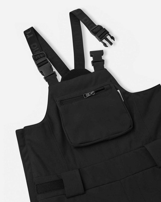 Close-up detail of the upper torso on the black Reima Rehti kids' snow bibs, highlighting the sturdy adjustable buckled suspenders, comfortable high-back design, and a secure zippered chest pocket for small essentials.