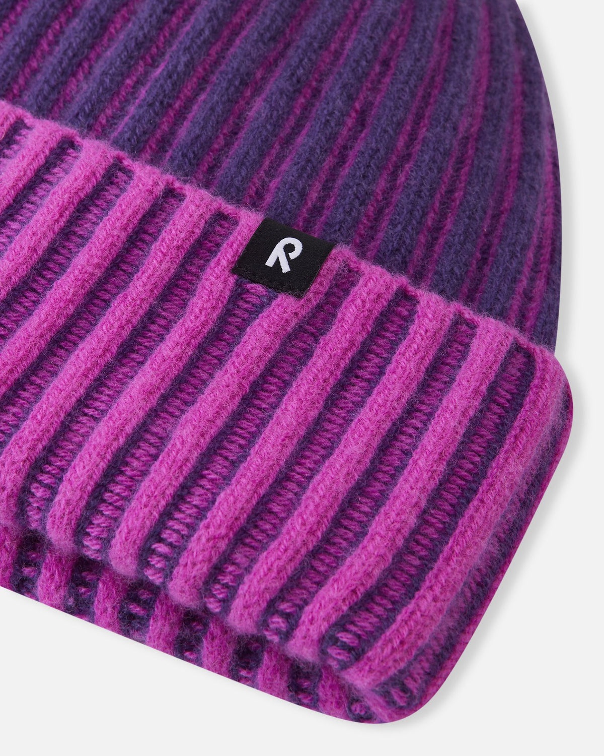 Detailed close-up of the Reima Veikee kids winter hat in plum purple, highlighting the thick, textured vertical ribbed knit construction of the 70% wool blend and the small black Reima 'R' logo patch sewn onto the cuff edge.