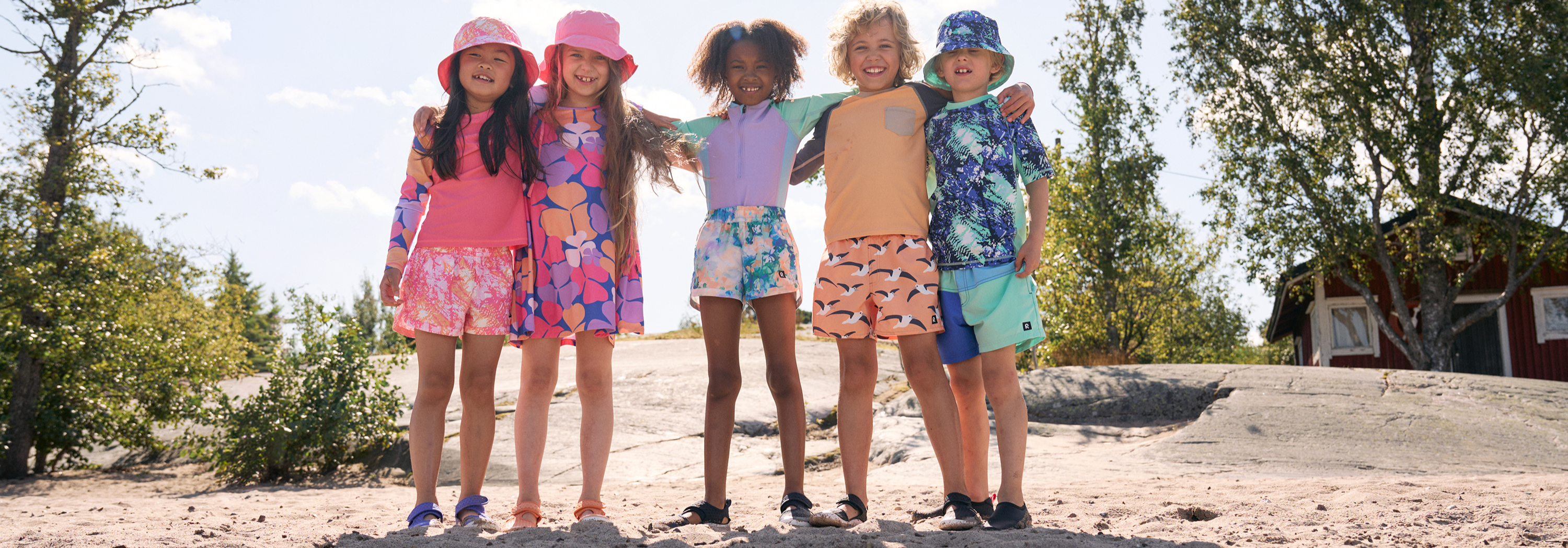 A group of kids modeling sun-protective summer beachwear, including floral swimsuits, colorful rash guards, and matching sun hats.