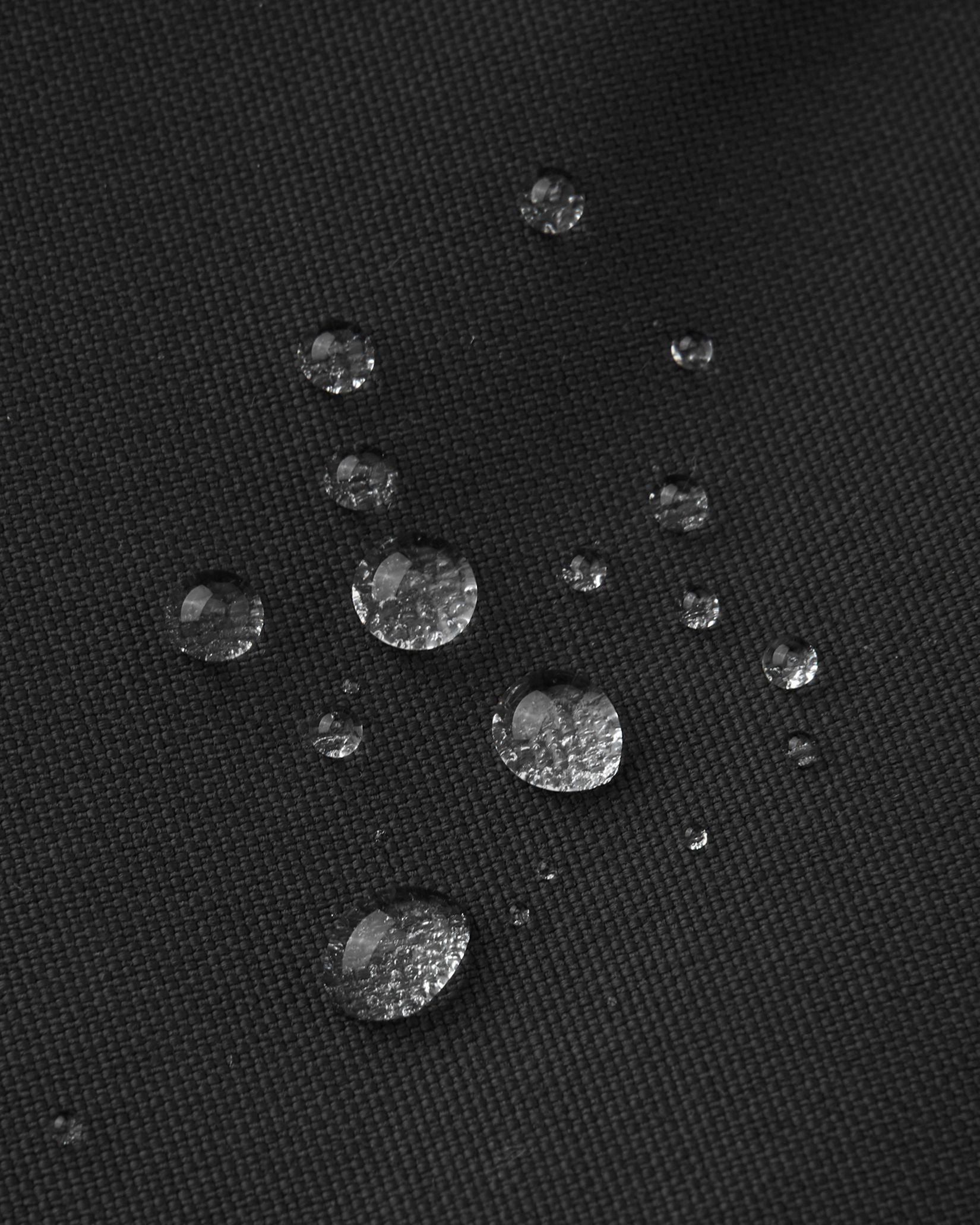 Macro close-up of water droplets perfectly beading on the black textured outer fabric of the Reima Alppi kids' snow bibs, visually highlighting the high-performance waterproof and dirt-repellent technology.