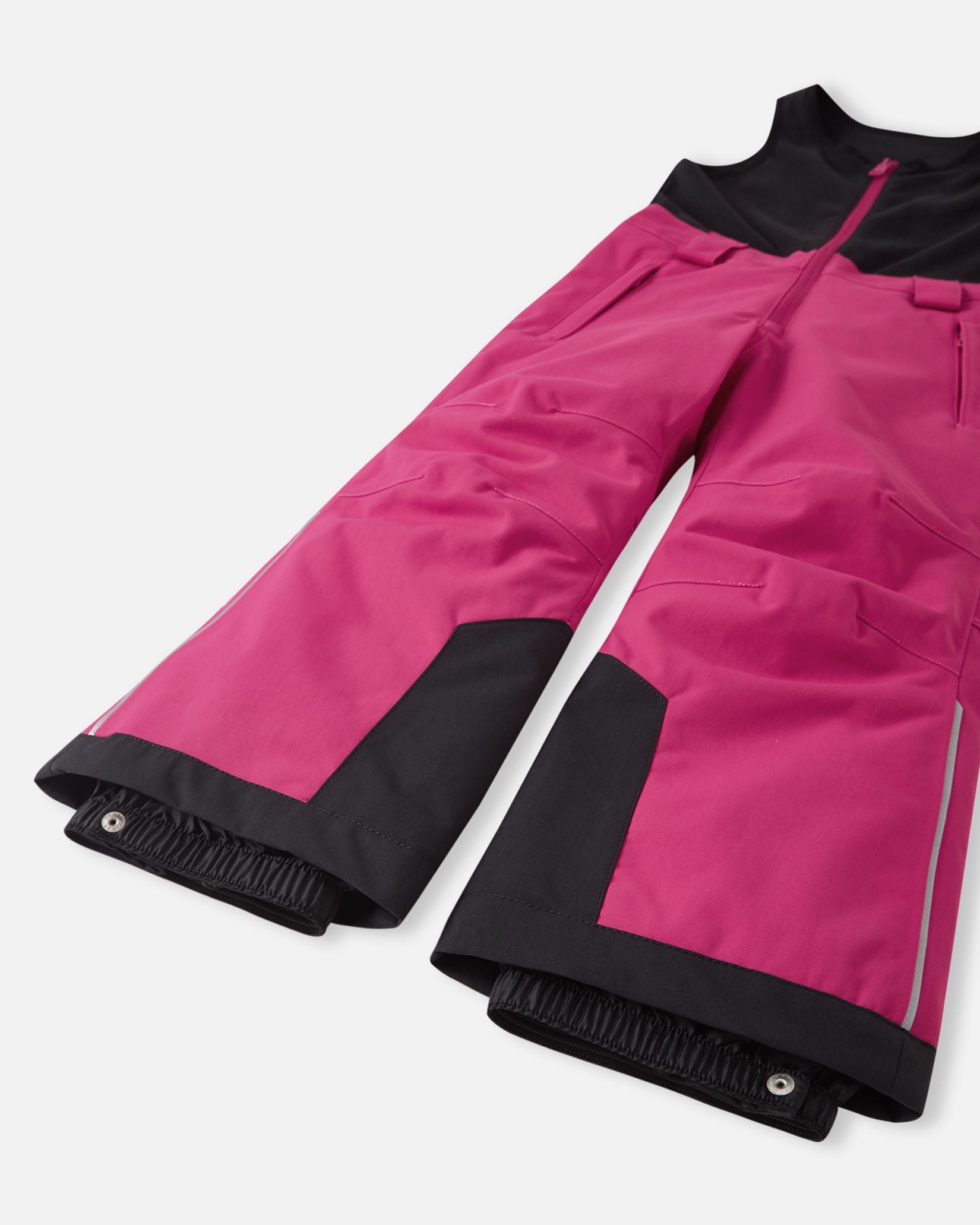 Detail view of the lower legs on the rosy berry Reima Alppi kids' snow pants, emphasizing the heavy-duty black reinforced hems and internal snow locks engineered to keep boots clear of deep snow.