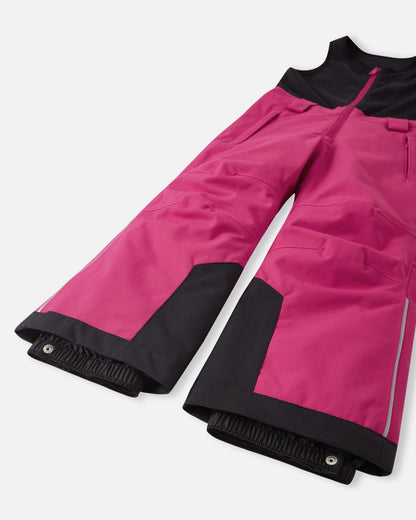 Detail view of the lower legs on the rosy berry Reima Alppi kids' snow pants, emphasizing the heavy-duty black reinforced hems and internal snow locks engineered to keep boots clear of deep snow.