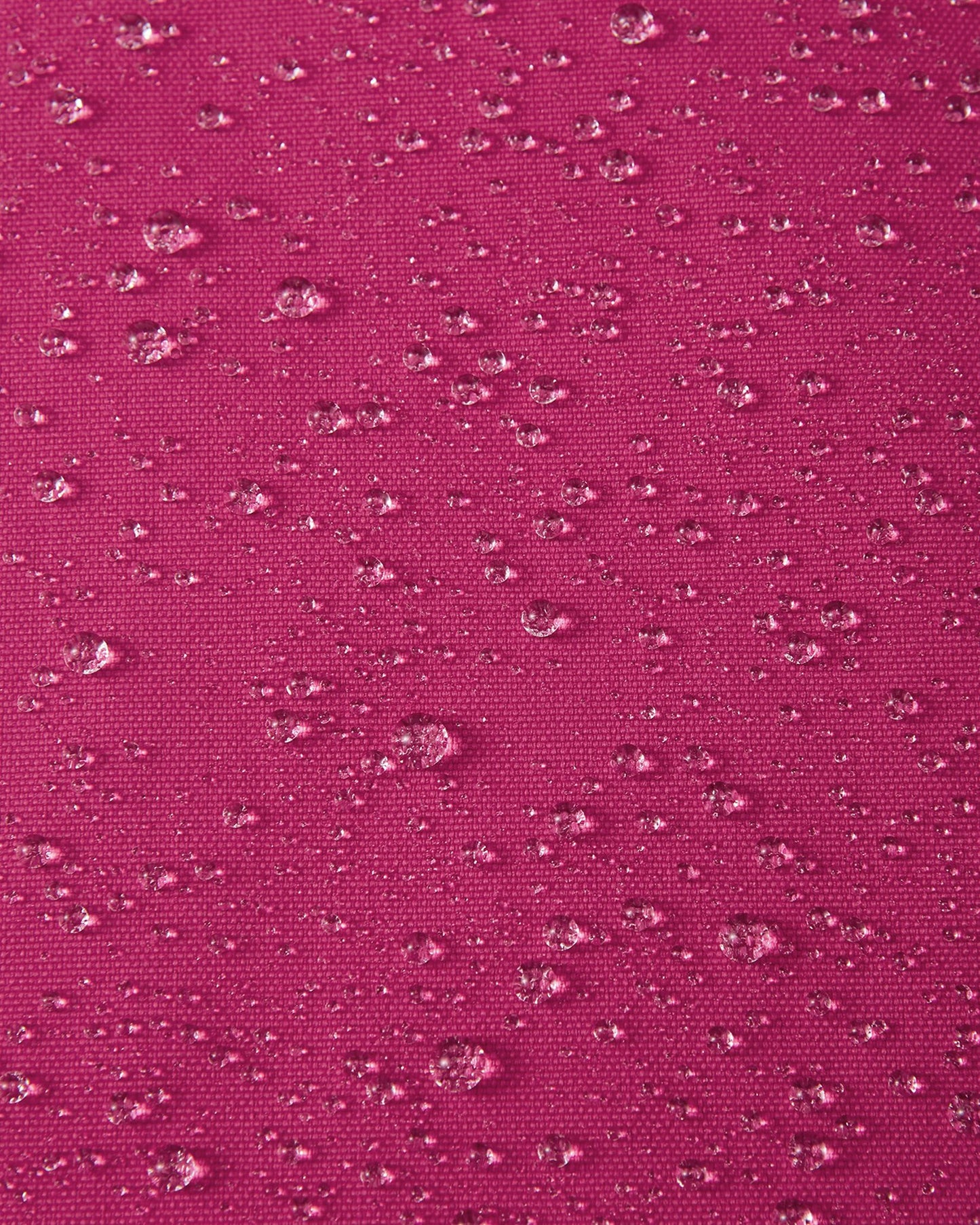Macro close-up of water droplets actively beading and rolling off the rosy berry pink outer shell of the Reima Alppi kids' snow bibs, demonstrating the highly effective Reimatec waterproof and breathable membrane.
