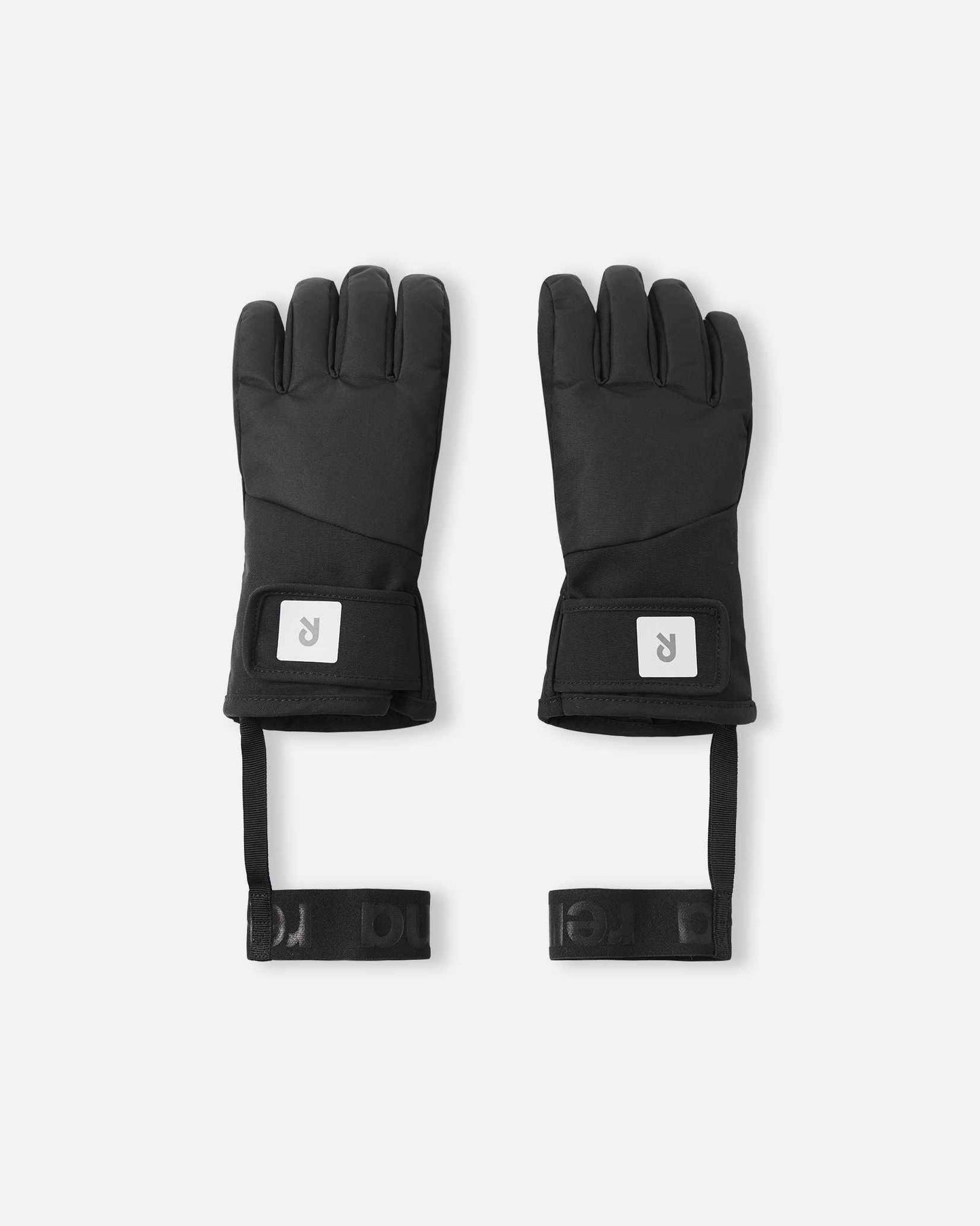 Flat lay view of the backs of the classic black Reima Hanskas kids' ski gloves. The image highlights the waterproof technical fabric, an easy-to-use hook-and-loop adjustable wrist strap for a secure fit, and attached elastic safety wrist leashes.