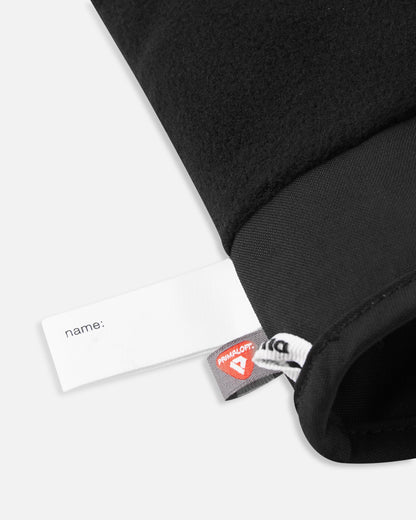 Close-up alternate detail of the interior of the black Reima Hanskas kids' ski gloves, clearly displaying a blank white customizable name tag and the recycled PrimaLoft insulation label attached to the cozy fleece lining.