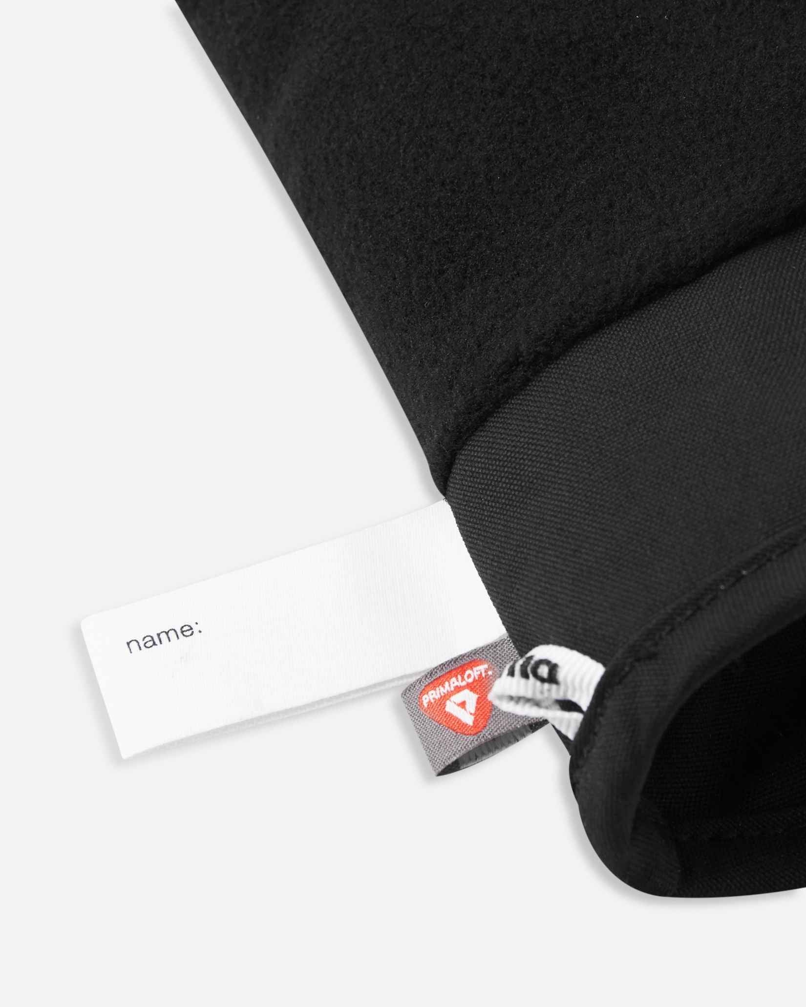 Detail of the inner cuff of the black Reima Hanskas kids' ski gloves, showing the soft thermal fleece lining, a customizable blank name tag, and the premium PrimaLoft insulation label indicating high-performance winter warmth.
