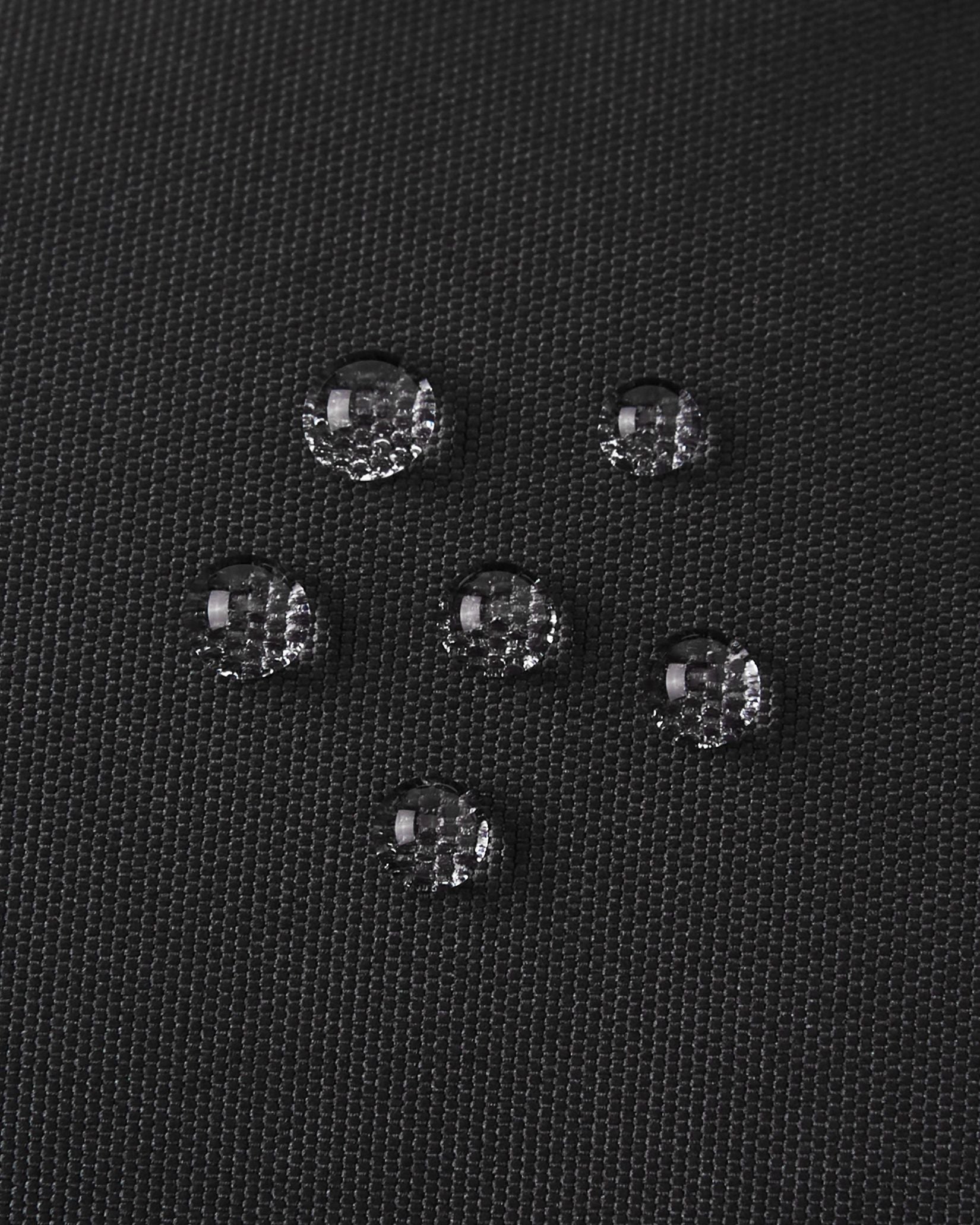 Detailed macro shot showing water beads resting perfectly on top of the black textured outer fabric of the Reima Hanskas kids' ski gloves, visually highlighting the highly effective water and dirt-repellent technology.