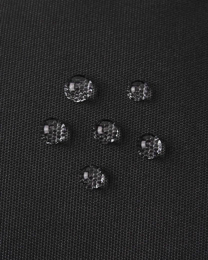 Detailed macro shot showing water beads resting perfectly on top of the black textured outer fabric of the Reima Hanskas kids' ski gloves, visually highlighting the highly effective water and dirt-repellent technology.
