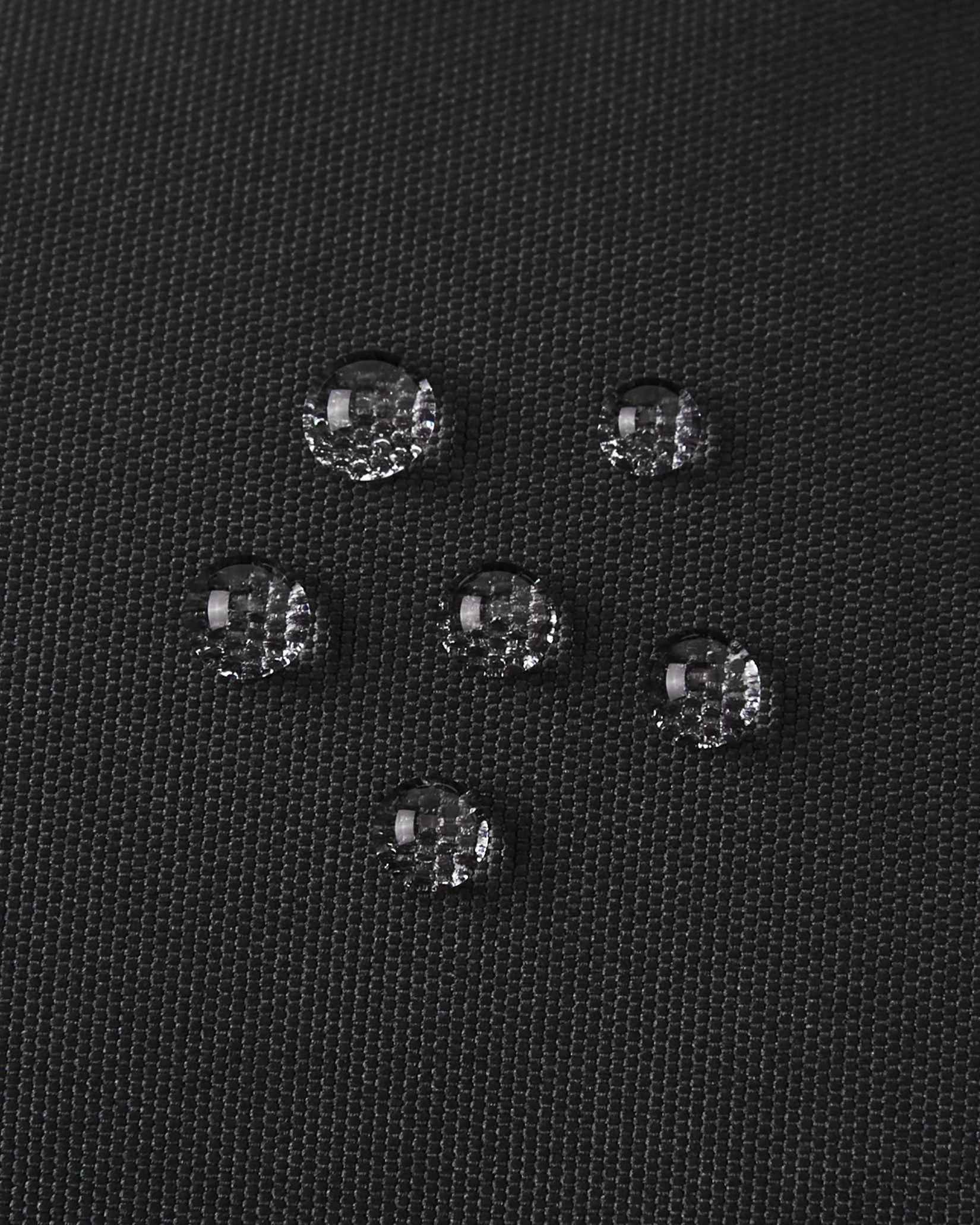 Macro close-up of water droplets actively beading and rolling off the black outer shell of the Reima Hanskas kids' ski gloves, demonstrating the high-performance waterproof and breathable technical membrane.