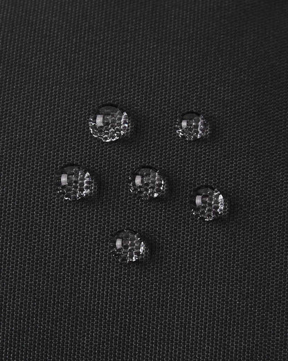 Macro close-up of water droplets actively beading and rolling off the black outer shell of the Reima Hanskas kids' ski gloves, demonstrating the high-performance waterproof and breathable technical membrane.