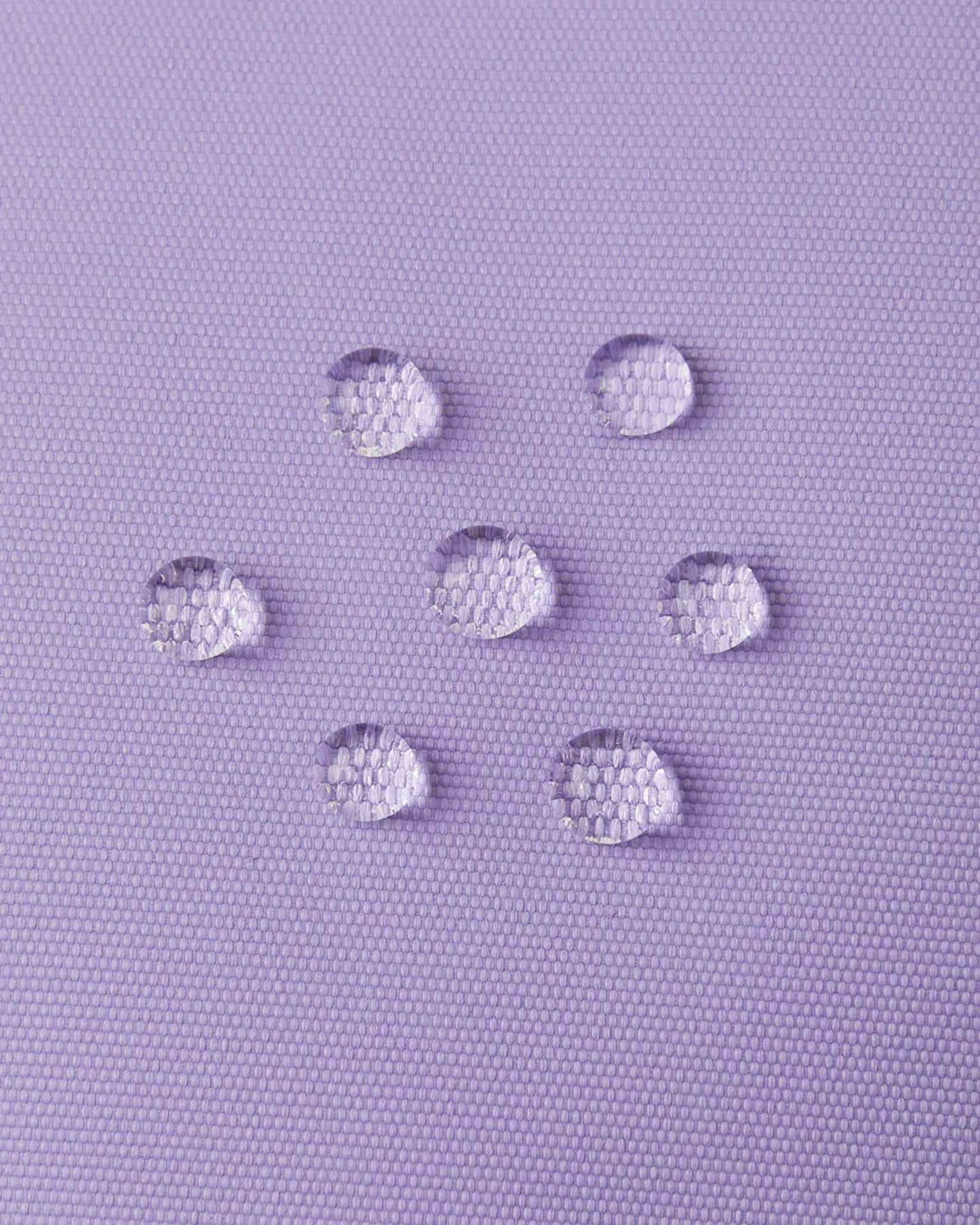 Macro close-up of water droplets beading and repelling off the blooming lilac purple outer fabric of the Reima Hanskas kids' ski gloves, demonstrating the high-performance waterproof technical membrane.
