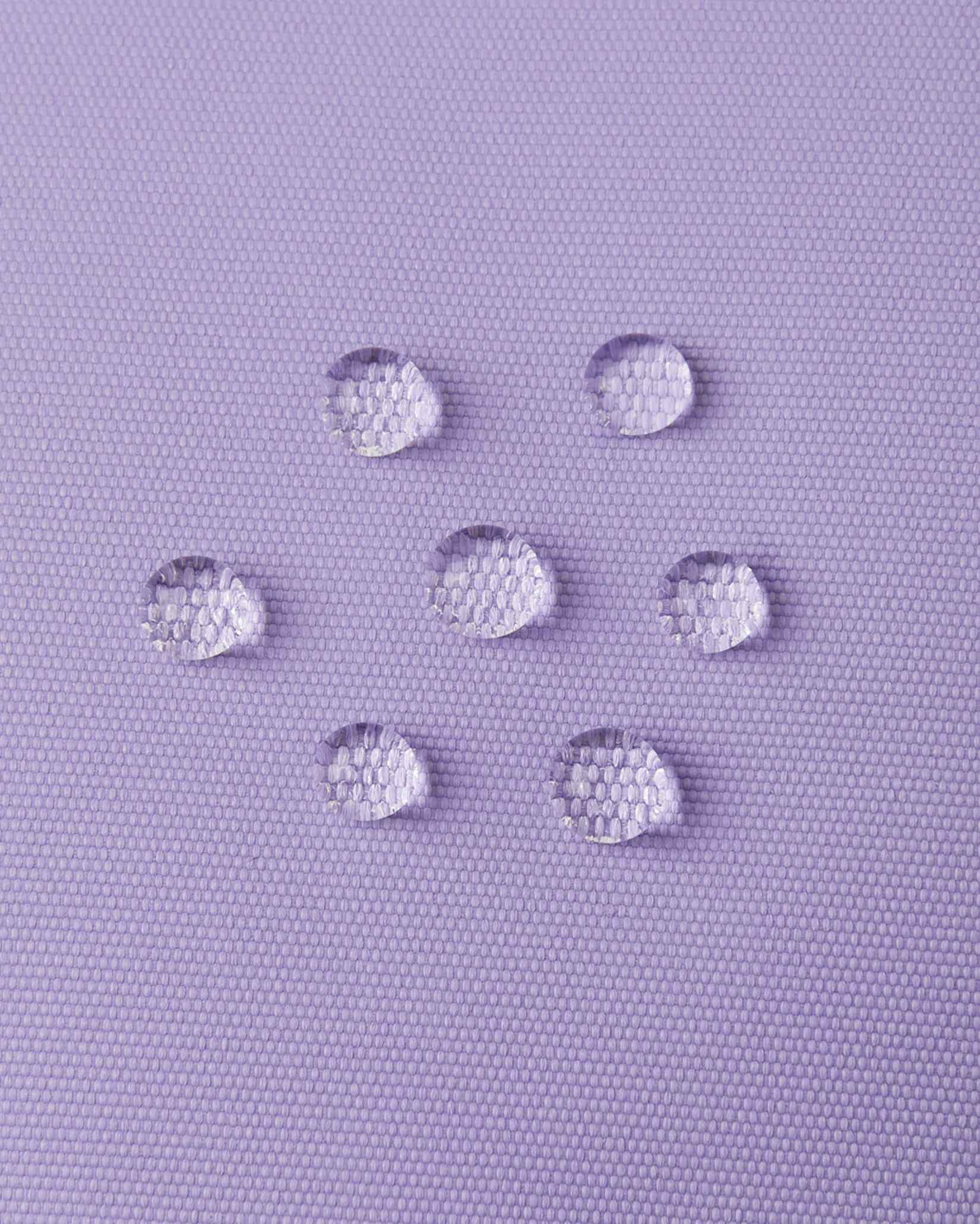 Macro close-up of water droplets beading and repelling off the blooming lilac purple outer fabric of the Reima Hanskas kids' ski gloves, demonstrating the high-performance waterproof technical membrane.