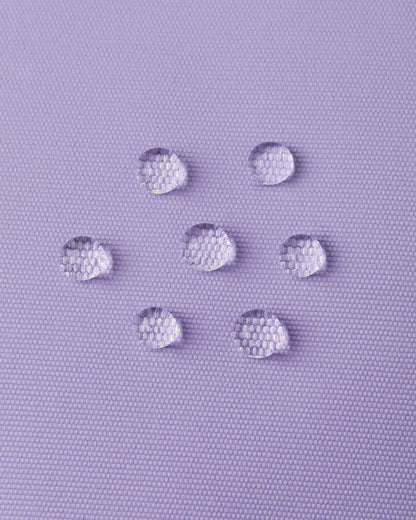 Macro close-up of water droplets beading and repelling off the blooming lilac purple outer fabric of the Reima Hanskas kids' ski gloves, demonstrating the high-performance waterproof technical membrane.