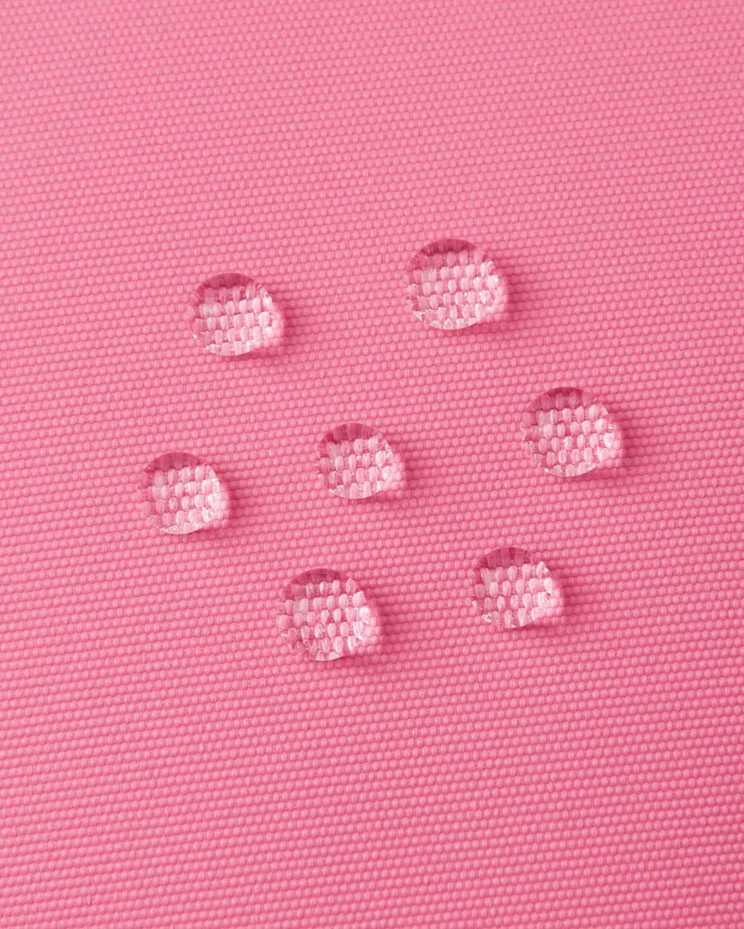 Macro close-up of water droplets actively beading and rolling off the soft coral outer shell of the Reima Hanskas kids' ski gloves, demonstrating the high-performance ReimaTec waterproof and breathable technical membrane.