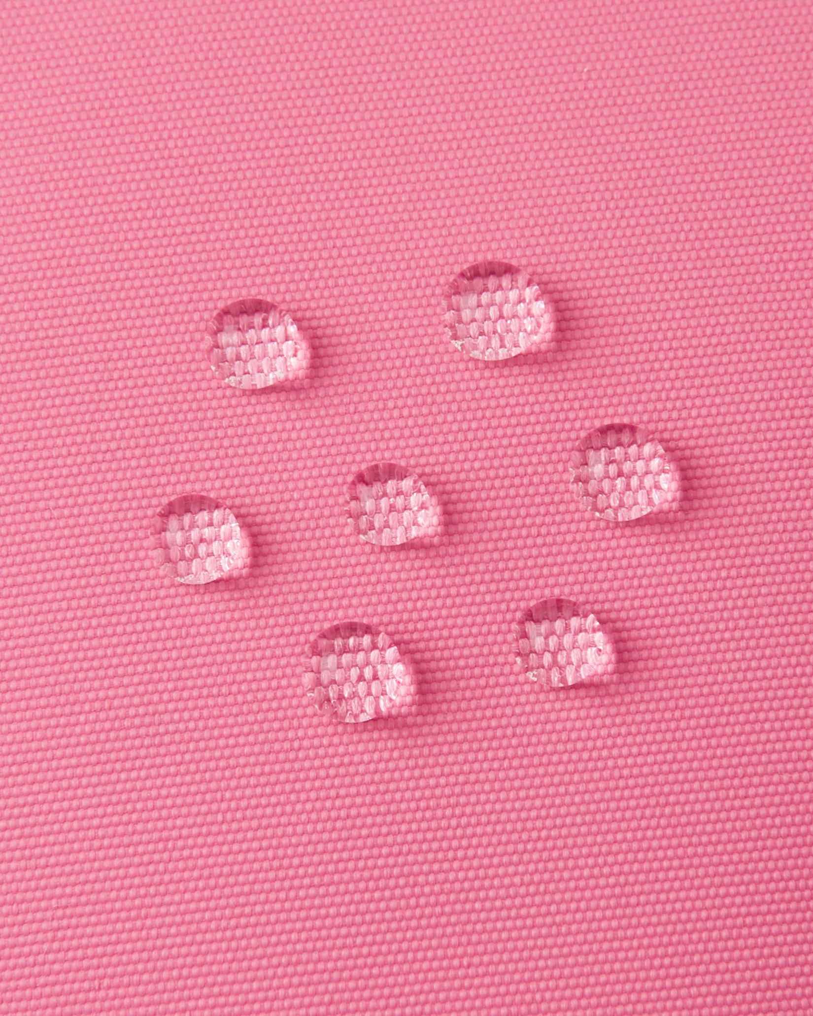 Macro close-up of water droplets actively beading and rolling off the soft coral outer shell of the Reima Hanskas kids' ski gloves, demonstrating the high-performance ReimaTec waterproof and breathable technical membrane.
