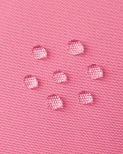 Macro close-up of water droplets actively beading and rolling off the soft coral outer shell of the Reima Hanskas kids' ski gloves, demonstrating the high-performance ReimaTec waterproof and breathable technical membrane.