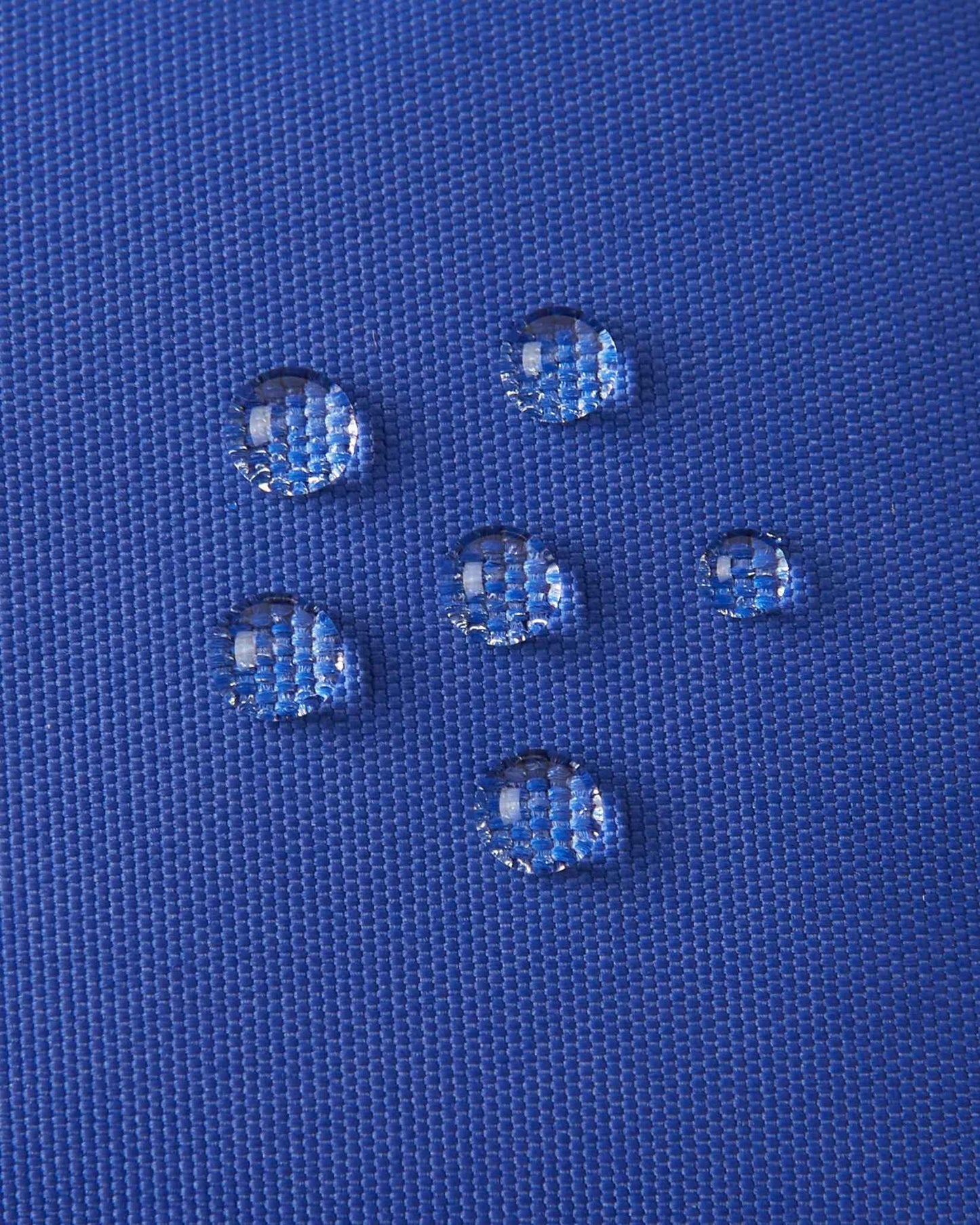 Macro close-up of water droplets actively beading and rolling off the twilight blue outer shell of the Reima Hanskas kids' ski gloves, demonstrating the high-performance waterproof Hipora insert and BIONIC-FINISH®ECO technical treatment.