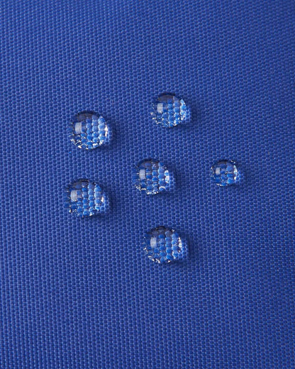 Macro close-up of water droplets actively beading and rolling off the twilight blue outer shell of the Reima Hanskas kids' ski gloves, demonstrating the high-performance waterproof Hipora insert and BIONIC-FINISH®ECO technical treatment.