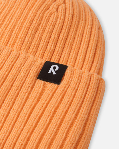 Close-up texture detail of the soft organic cotton ribbed knit on the apricot Reima Hattara kids' beanie, showing the contrast black-and-white logo tag.
