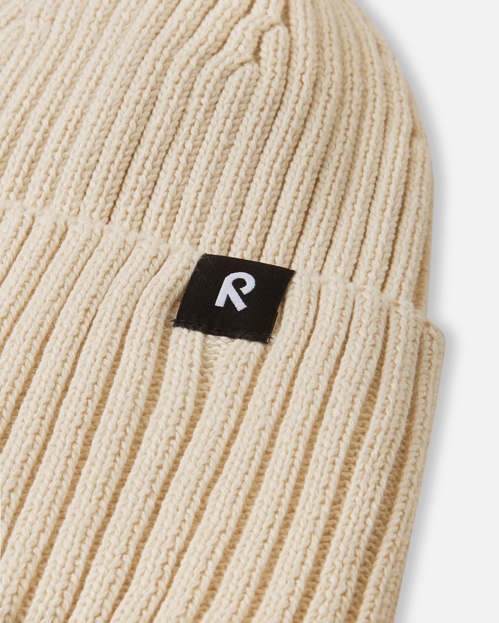 Macro close-up of the soft, breathable organic cotton ribbed knit fabric used on the birch beige Reima Hattara kids' beanie.