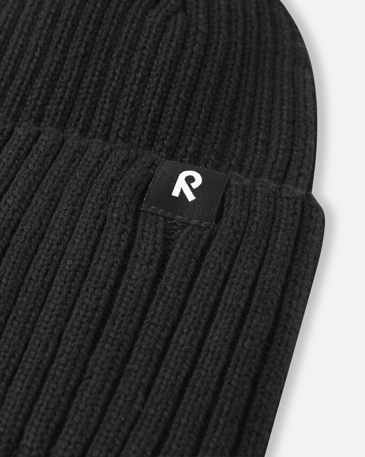 Close-up of the branded logo tag on the black Reima Hattara kids' organic cotton beanie, highlighting the clean stitching and premium ribbed knit quality.