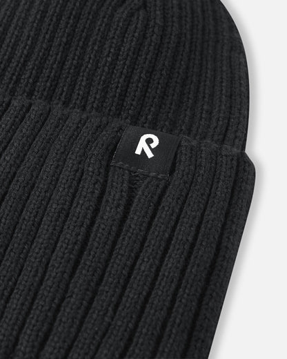 Close-up of the branded logo tag on the black Reima Hattara kids' organic cotton beanie, highlighting the clean stitching and premium ribbed knit quality.