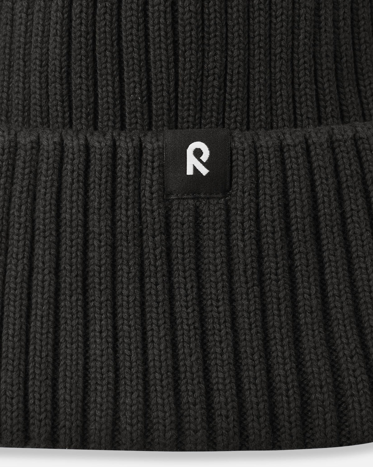 Macro close-up of the soft, breathable organic cotton ribbed knit fabric used on the black Reima Hattara kids' beanie.