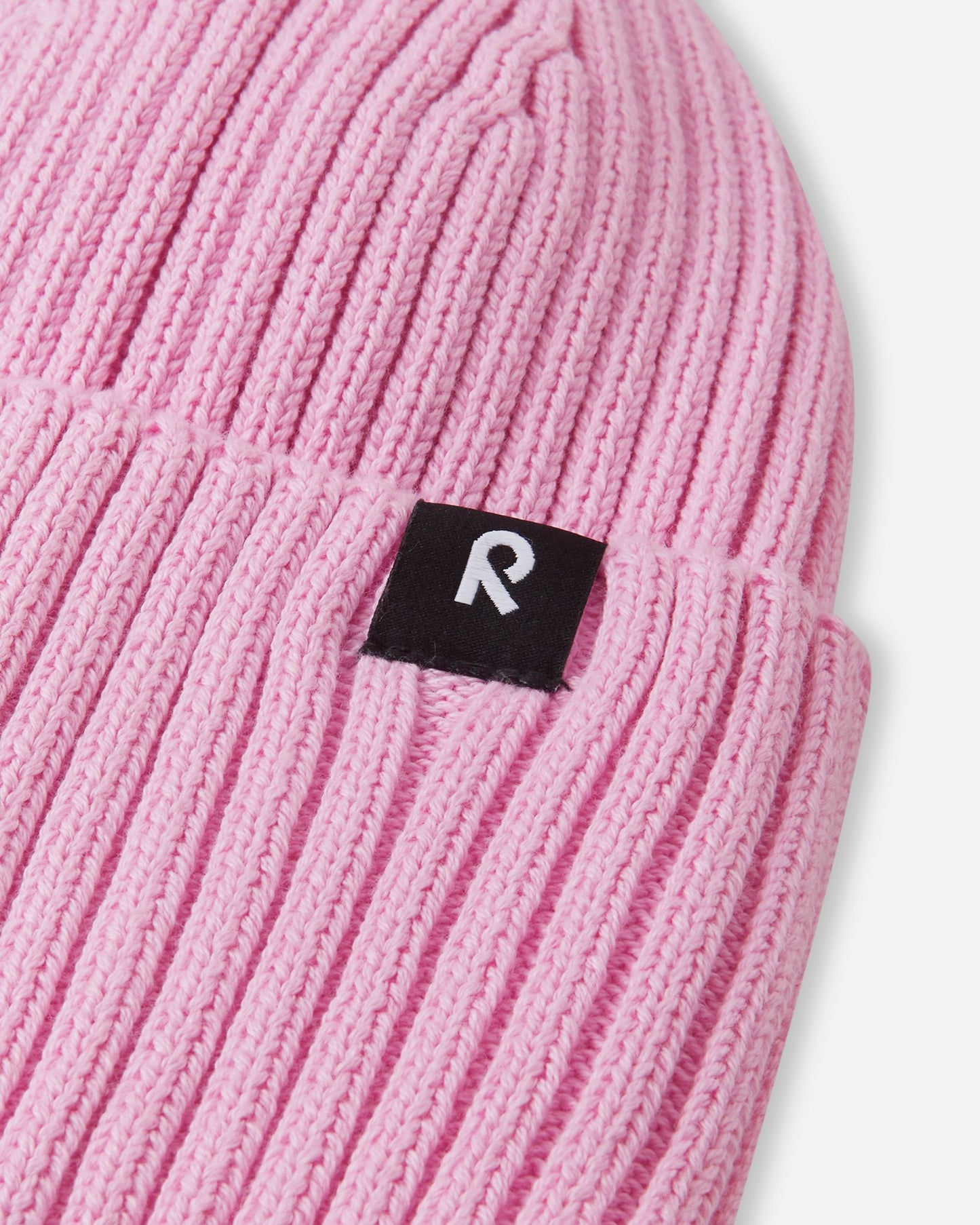 Close-up texture detail of the soft organic cotton ribbed knit on the light heather pink Reima Hattara kids' beanie, highlighting the contrast Reima logo patch.