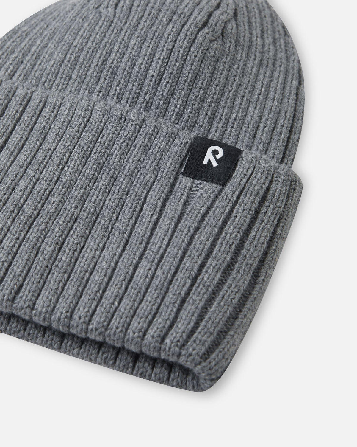 Close-up texture detail of the soft organic cotton ribbed knit on the melange grey Reima Hattara kids' beanie, highlighting the contrast Reima logo patch.