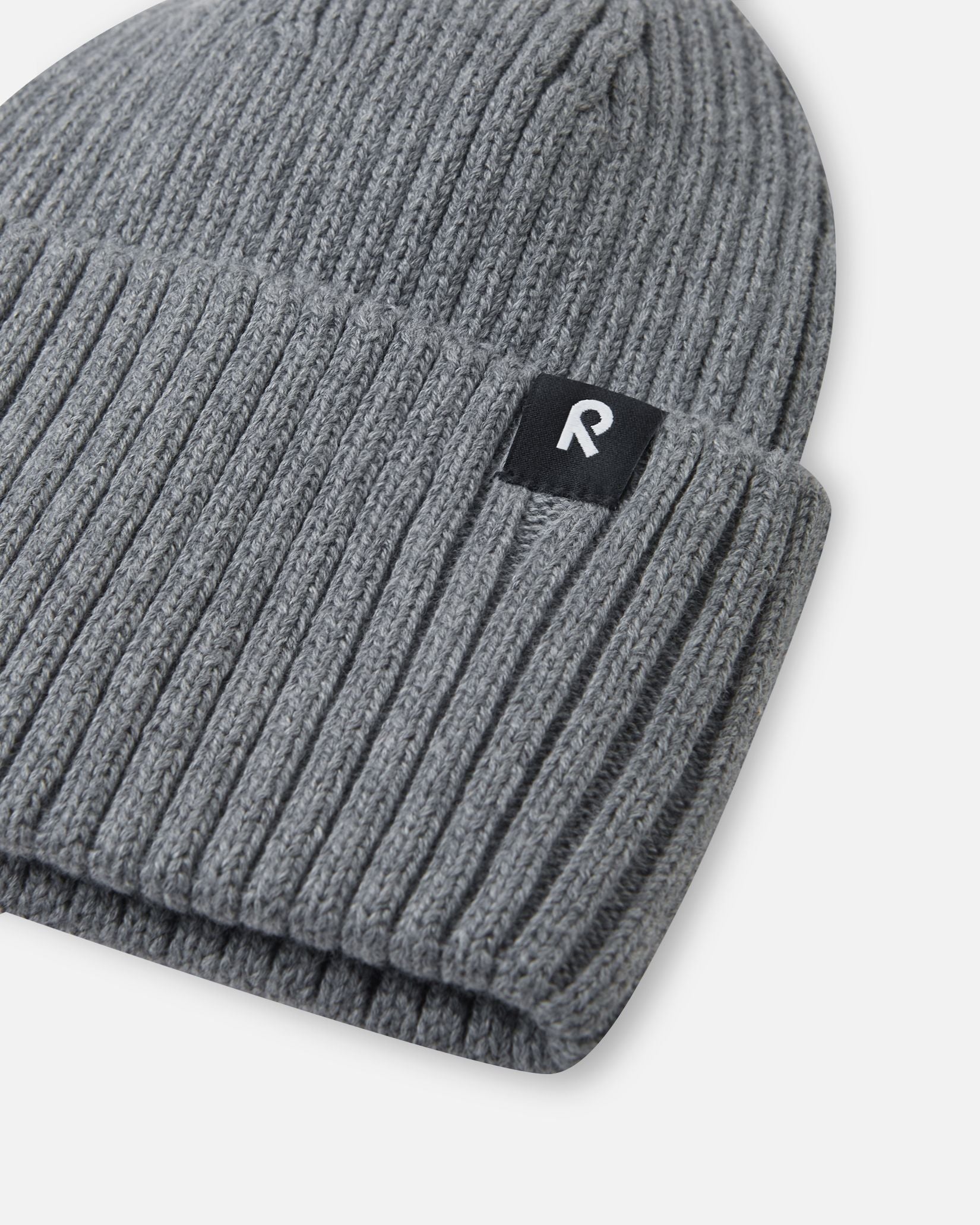 Close-up texture detail of the soft organic cotton ribbed knit on the melange grey Reima Hattara kids' beanie, highlighting the contrast Reima logo patch.