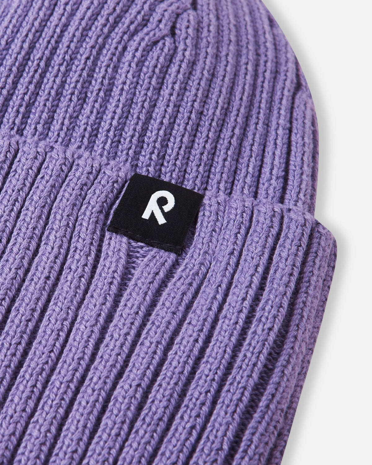 Close-up texture detail of the soft organic cotton ribbed knit on the misty violet Reima Hattara kids' beanie, highlighting the contrast logo patch.