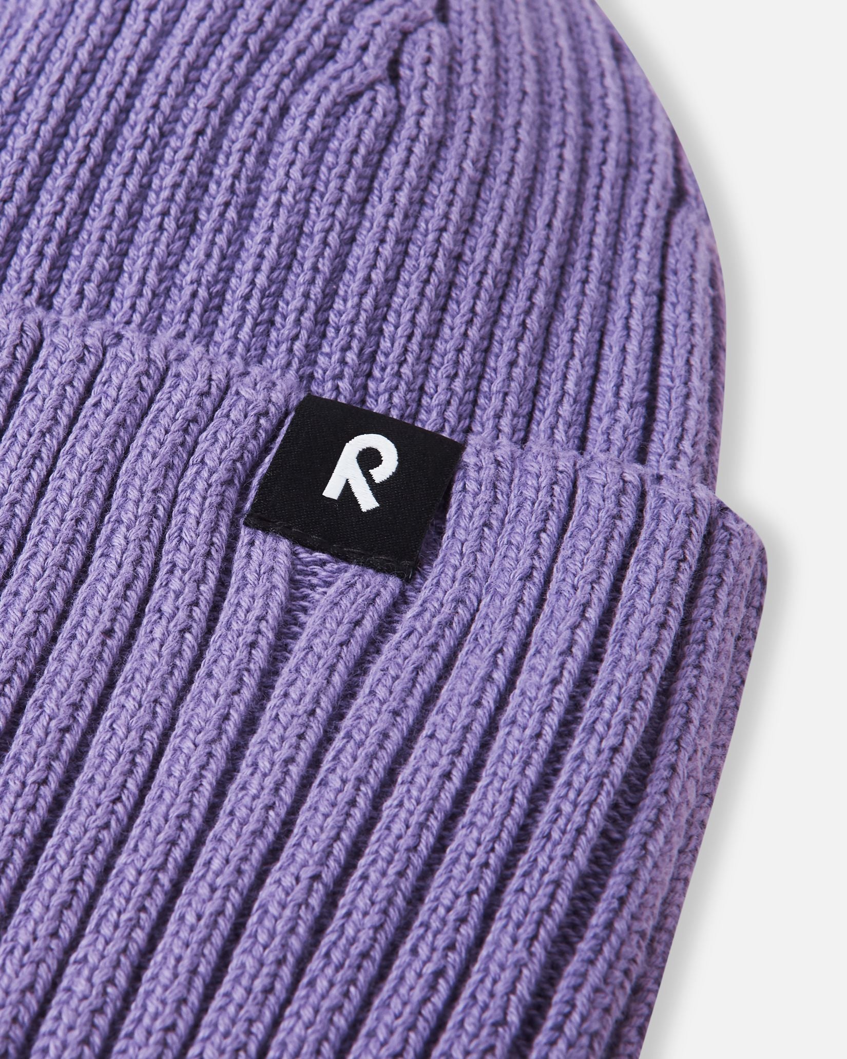 Close-up texture detail of the soft organic cotton ribbed knit on the misty violet Reima Hattara kids' beanie, highlighting the contrast logo patch.
