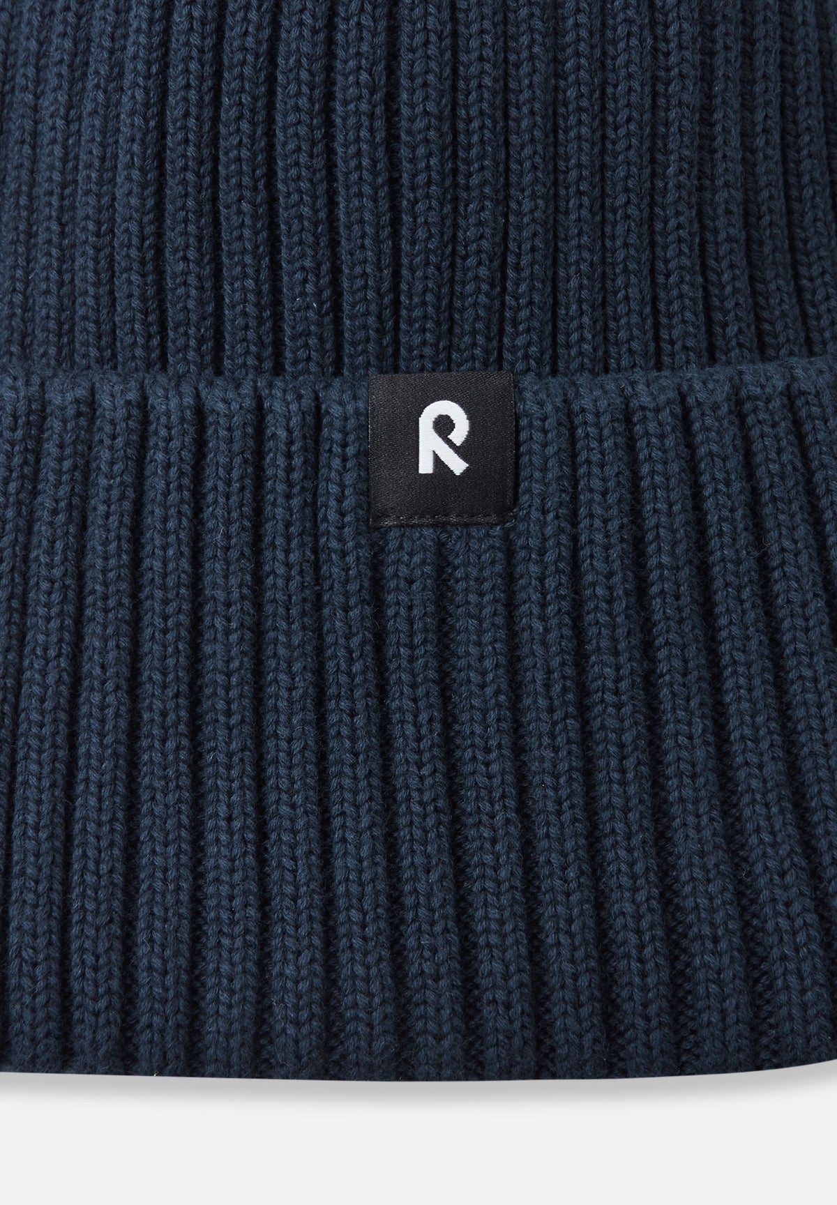 Macro close-up of the soft, breathable organic cotton ribbed knit fabric used on the navy Reima Hattara kids' beanie, featuring the branded logo patch.