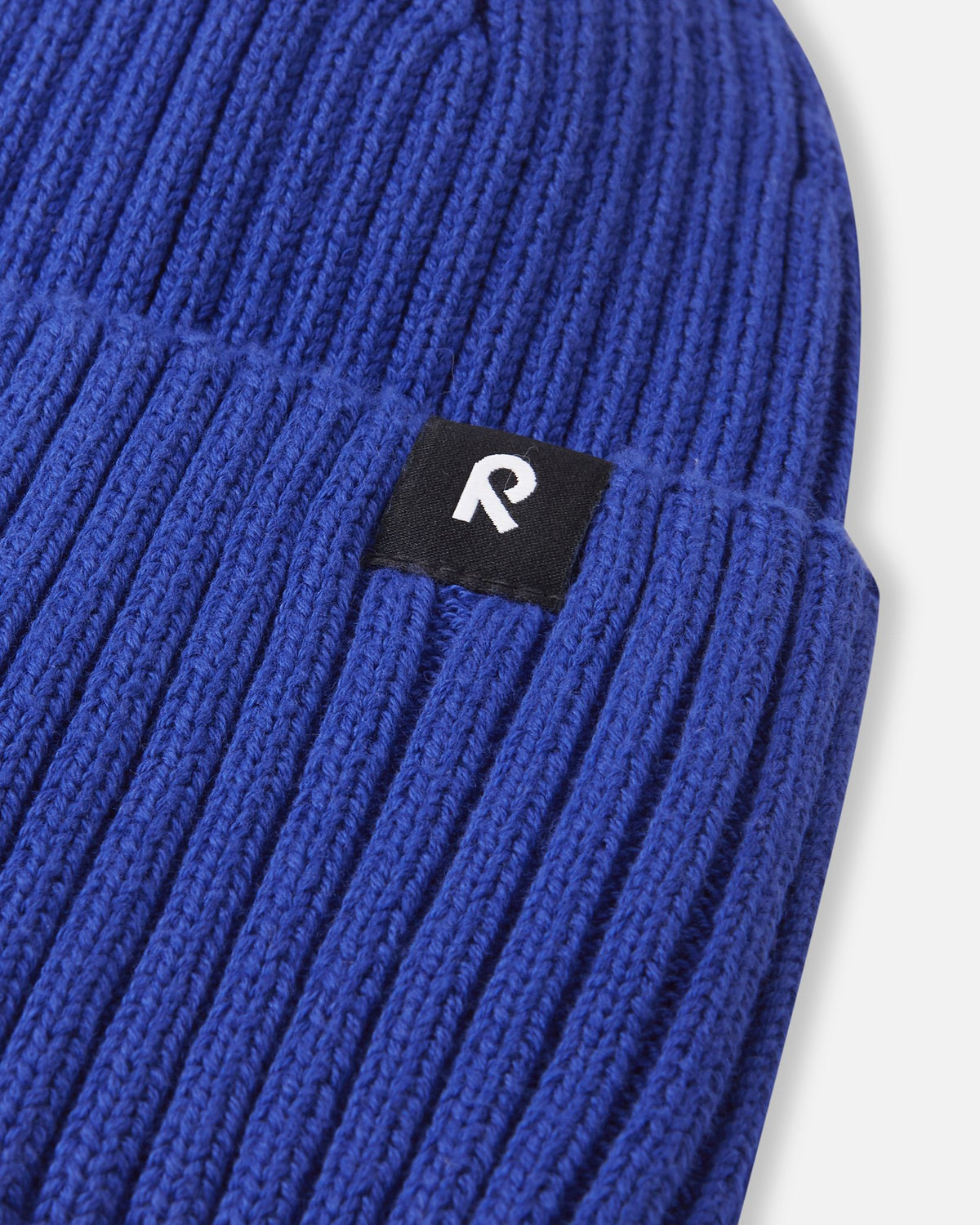 Close-up texture detail of the soft organic cotton ribbed knit on the sparkly blue Reima Hattara kids' beanie, highlighting the contrast Reima logo patch.