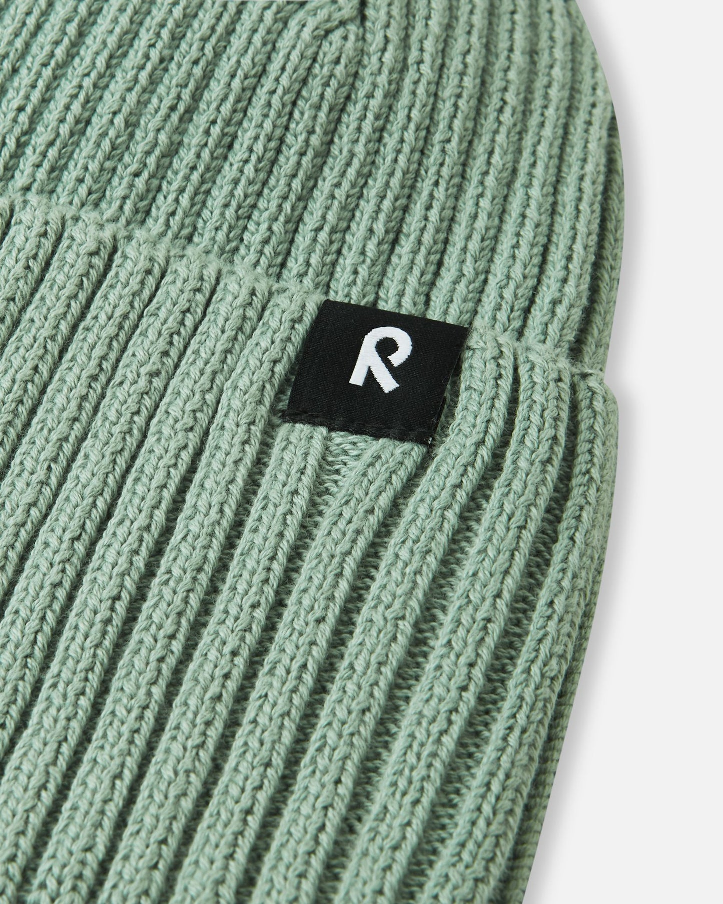 Macro close-up of the soft, breathable organic cotton ribbed knit fabric used on the stone green Reima Hattara kids' beanie.