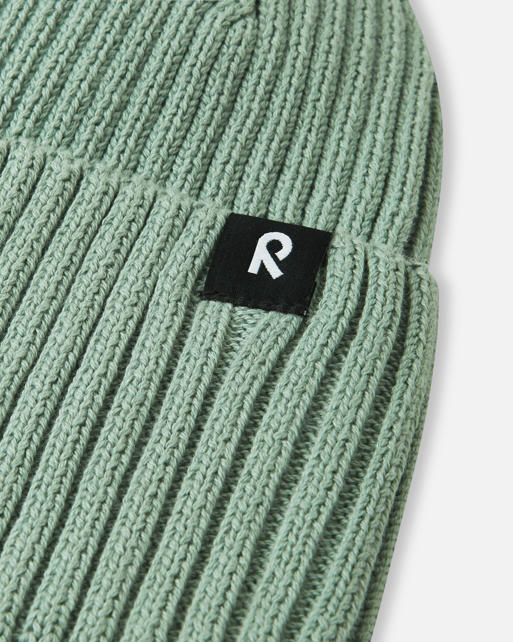 Macro close-up of the soft, breathable organic cotton ribbed knit fabric used on the stone green Reima Hattara kids' beanie.