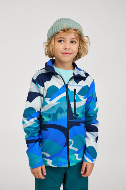 Lifestyle shot of a young child wearing the stone green Reima Hattara kids' organic cotton beanie paired with a colorful printed softshell jacket, demonstrating its comfortable everyday outdoor wear fit.