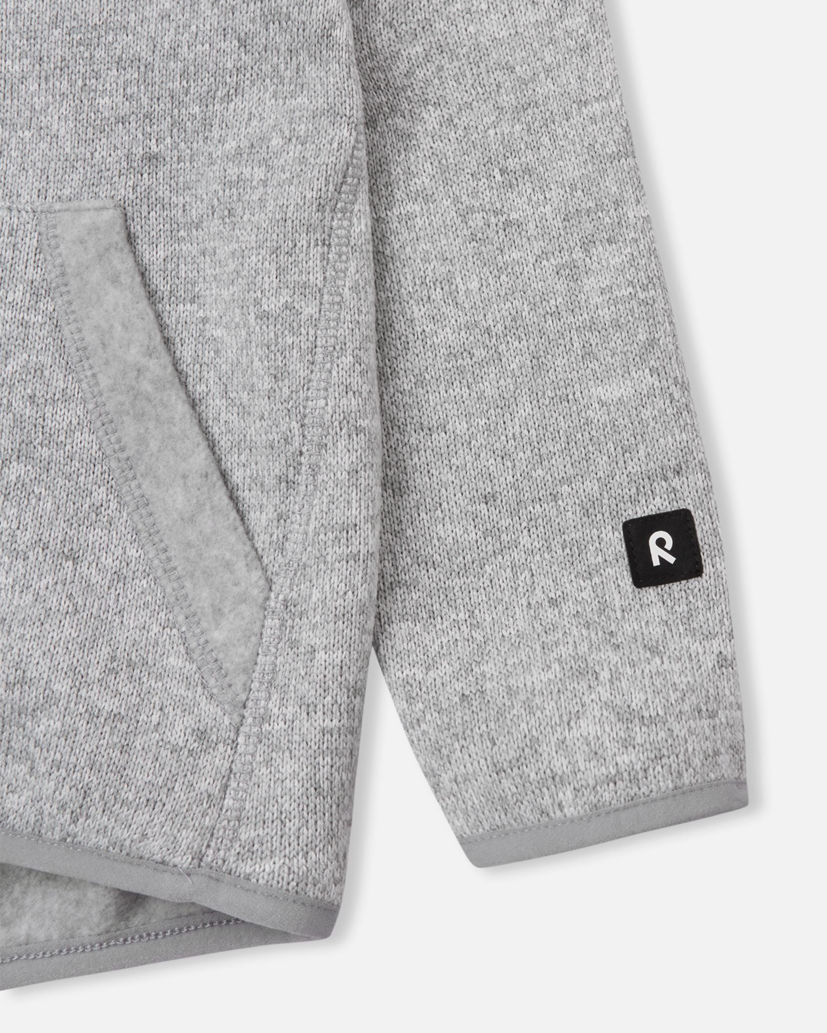 Close-up of the ribbed sleeve cuff and branded black Reima logo patch on the melange grey Reima Hopper kids' knit fleece jacket.