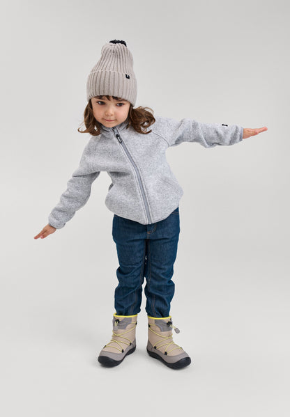 Lifestyle photo of a child modeling the melange grey Reima Hopper kids' knit fleece jacket with arms outstretched, styled with a winter beanie, jeans, and boots to showcase active everyday wear and fit.