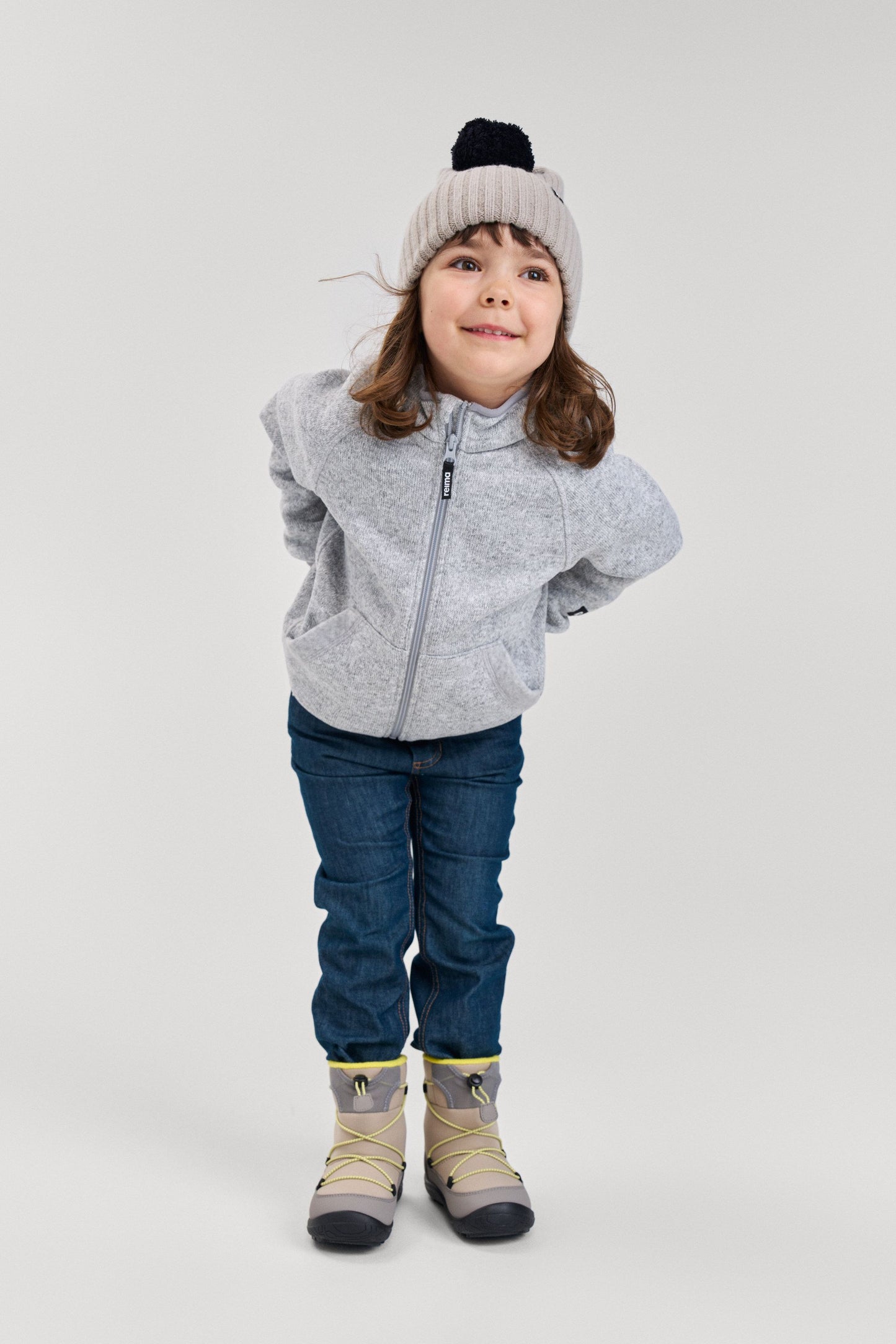 Lifestyle shot of a young child wearing the melange grey Reima Hopper kids' knit fleece jacket paired with jeans and winter boots, demonstrating its versatile and comfortable everyday outdoor fit.