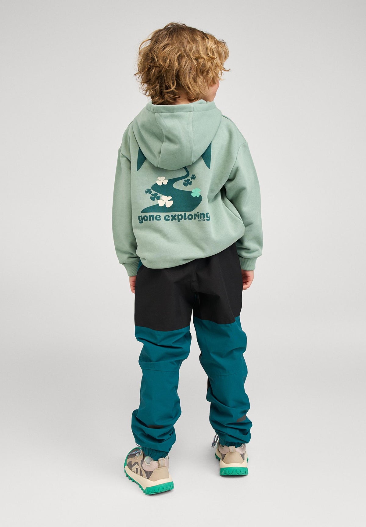 Lifestyle shot from the back of a child wearing the stone green Reima Huppis hoodie, clearly showing the large "gone exploring" graphic and the comfortable drape of the organic cotton fabric.