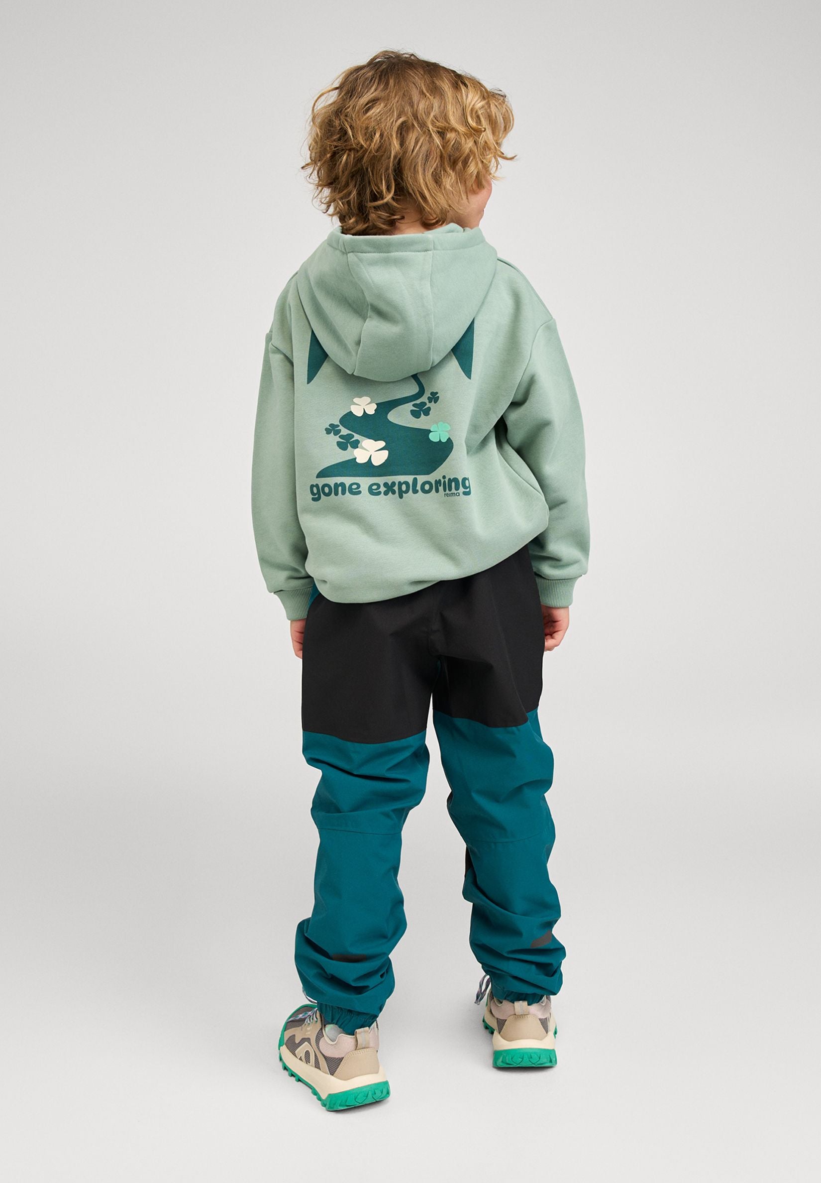 Lifestyle shot from the back of a child wearing the stone green Reima Huppis hoodie, clearly showing the large "gone exploring" graphic and the comfortable drape of the organic cotton fabric.
