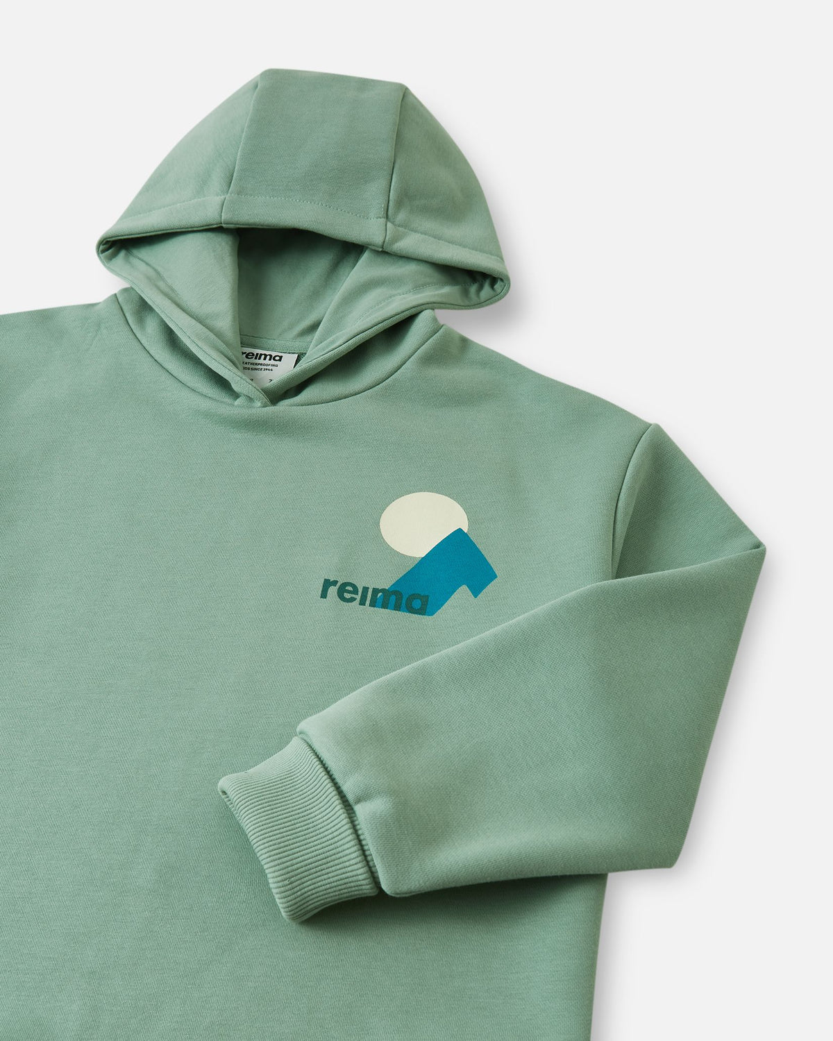Detailed close-up of the stone green Reima Huppis kids' hoodie, focusing on the comfortable lined hood, the geometric chest graphic, and the securely ribbed sleeve cuff.