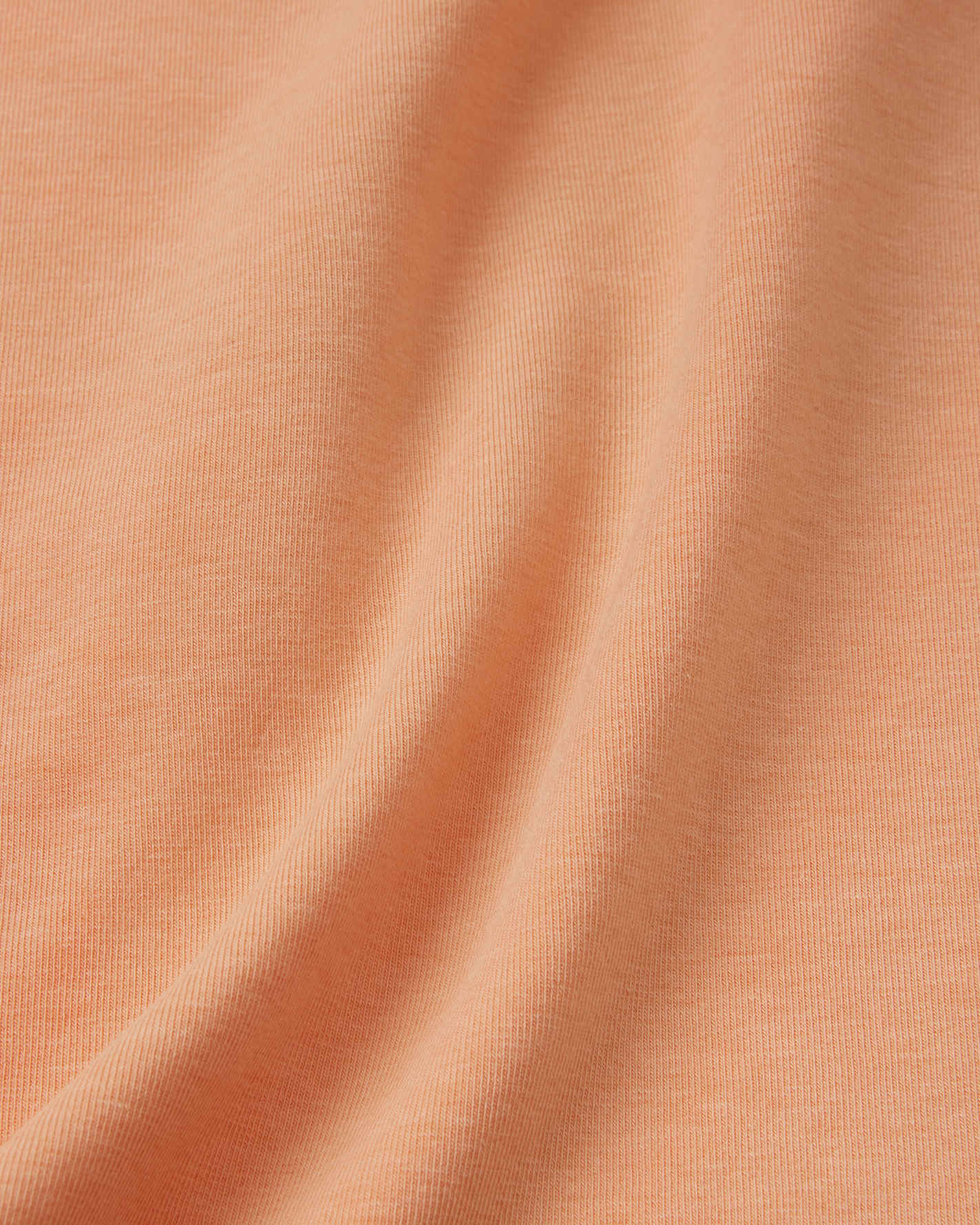 Macro close-up of the soft, breathable UPF 50+ fabric used in the apricot Reima Ikioma kids' summer t-shirt, highlighting its smooth, lightweight knit texture designed to keep children cool.