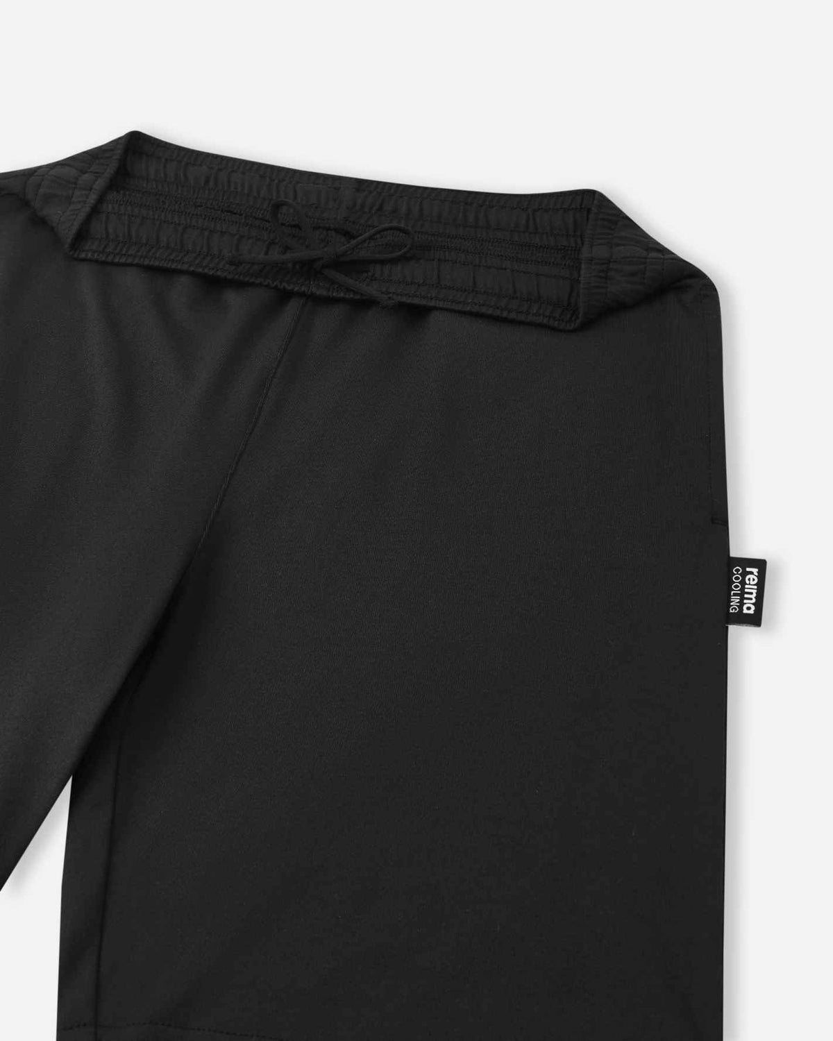 A close-up view of the gathered elastic waistband and black adjustable drawstring on the black Reima Ilmassa shorts. A small black Reima logo tag is visible on the side seam.